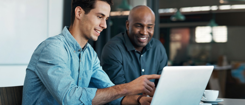 Two men in a conference room looking at something on a laptop, focused on the screen.